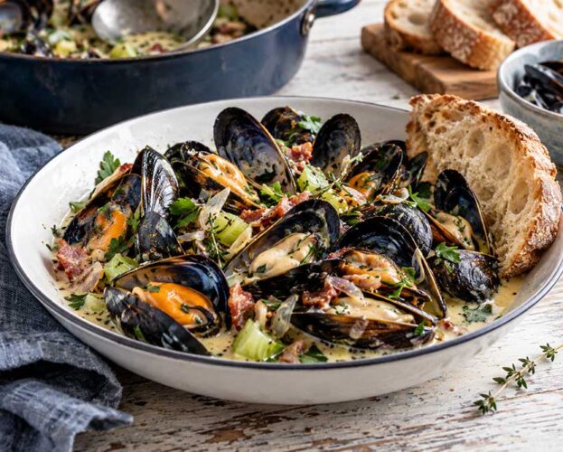 Bowl of mussels with ale, smoked bacon and thyme in a creamy mustard broth with parsley and crusty bread