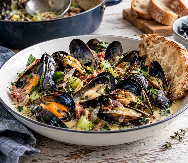 Bowl of mussels with ale, smoked bacon and thyme in a creamy mustard broth with parsley and crusty bread
